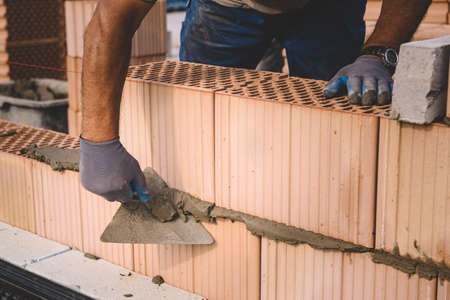 Professional construction worker laying bricks and mortar - building house wallの写真素材