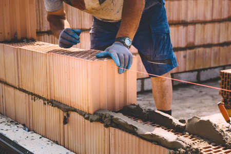 Professional construction worker laying bricks and mortar - building house wall