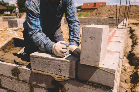 Professional construction worker laying bricks and mortar - building house wall
