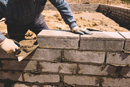 Professional construction worker laying bricks and mortar - building house wall