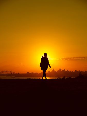 Sunset over Sydney, Australia with a woman standing in front of the sun enjoying the viewの写真素材