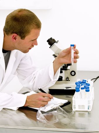 Male scientist looking at the flask with a microscope behind himの写真素材