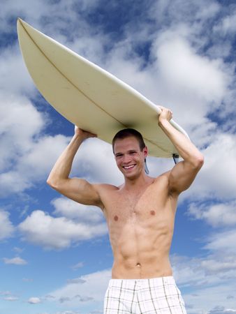 Muscular surfer dude walks with his surfboard over his headの写真素材