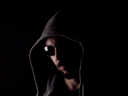 Low key image of a bearded man with a hoody and sunglasses