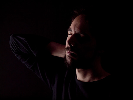 Low key image of a bearded man with a sore neck