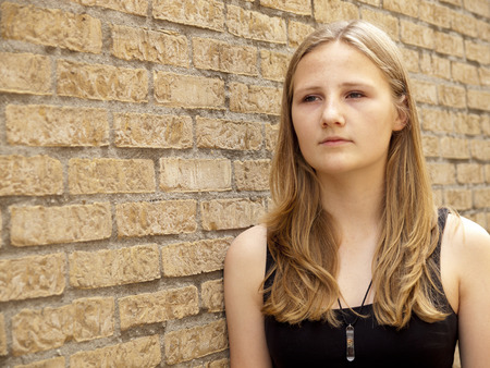 Young teenage girl looking sad or depressed in front of a brick wall backgroundの写真素材
