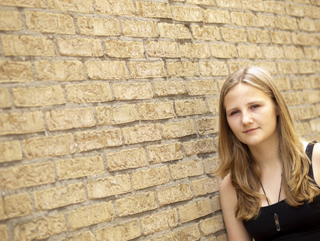 Young teenage girl looking sad or depressed in front of a brick wall backgroundの写真素材