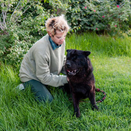 A blond man wearing a green sweater playing and petting his black dog in a green area of his houseの写真素材
