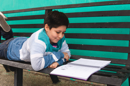 Elementary school boy is reading a book on the park bench. The boy is in elementary school. Boy studying outsideの写真素材