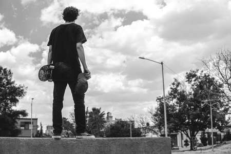 A skater is standing on a park ramp with his board about to do a trick. The boy is looking into the distance. You see the sky in the backgroundの写真素材