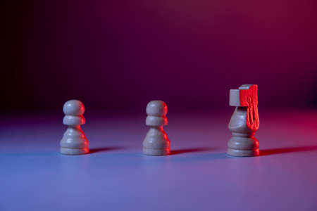 Two pawns and a chess knight arranged on a purple background with lights. Chess pieces. Red light on the right side. Detail shot of the chess piece.の写真素材