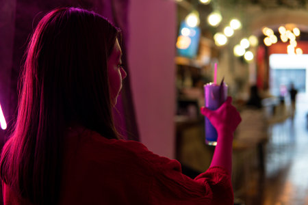 Hispanic girl in a red dress from the back in a room with pink neon light with a nightclub in the...