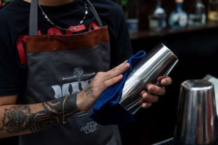 Body of an unrecognizable bartender while he cleans one of his work utensils with a rag.の写真素材