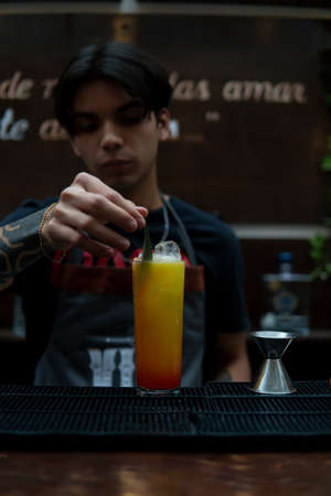 Waiter preparing a yellow drink that looks like juice, he is placing a small leaf on it as decoration.の写真素材