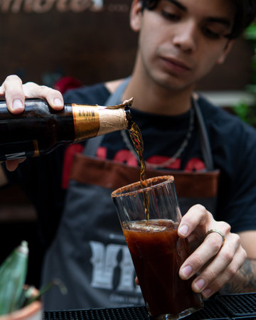 Hispanic young barman pouring a bottle of beer into a glass to prepare an alcoholic drink.の写真素材