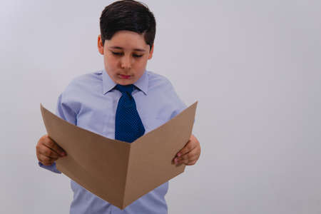 A boy dressed in a suit and tie pretending to be a businessman while reading a folder with important papers. A little boy dressed as a businessman.の写真素材