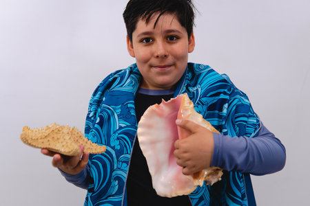 Boy dressed in beach clothes on isolated white background holding a shell and starfish. Boy with...