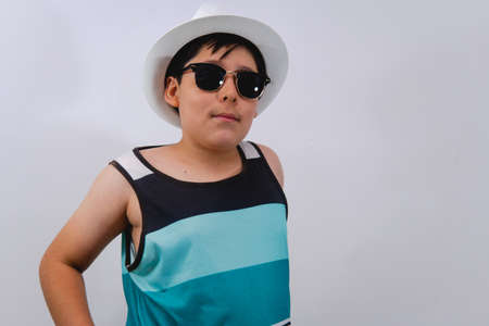Little boy on an isolated white background dressed in a blue tank top, a white hat, and blue glasses. Beach boy on white background.の写真素材