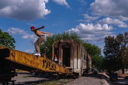 Latin fitness man on an abandoned train. Hispanic man about to do a somersault. Latino boy practicing stunts in a park with abandoned rusty machines. Athletic man practicing parkour.の写真素材