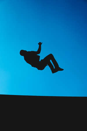Silhouette of a man who is against the light while doing a somersault with the sky in the...