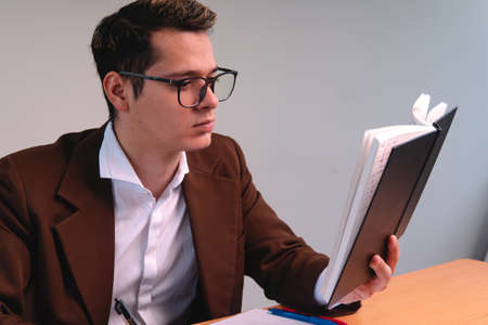 Portrait of a man dressed in a suit reading. Business man on a white background. Blond man reading the notes in his notebook. Blond boy dressed in brown suit, shirt and glasses. High quality photoの写真素材