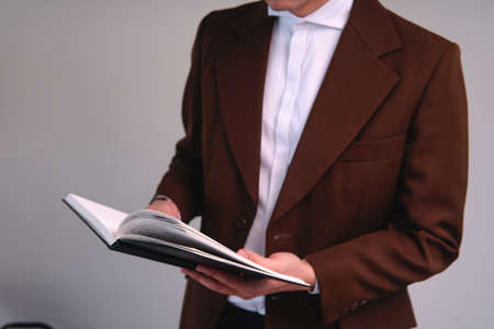 Unrecognizable man dressed in brown suit with a book in his hands. body shot of a businessman with a...