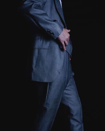 Waist of a man in a suit on a black background. Gray colored suit of an elegant man walking. Unrecognizable man in brown suit walking on dark background. High quality photoの写真素材