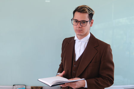 Teacher in front of the class explaining a topic. An elegant man giving a class. University professor with a book in his hand. High quality photoの写真素材