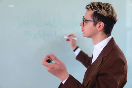 A university professor sketching in the middle of a class on the whiteboard. Elegant man in suit...
