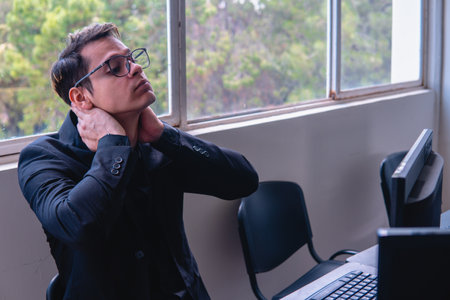 Tired office worker after a day of work. Man at a desk craning his neck. Office worker working on the computer at his desk. High quality photoの写真素材
