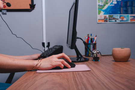 Close up to a work desk with the computer, keyboard and mouse. Womans hands working at her desk. High quality photoの写真素材