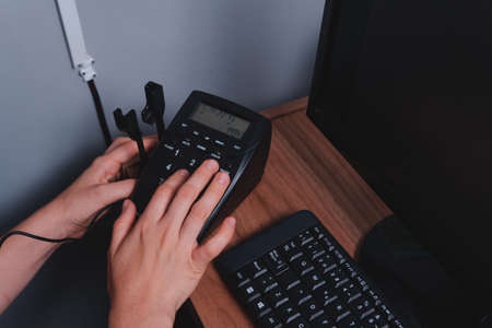 Close up of a hand typing a phone number at a desk in an office. Woman in call center dialing a...
