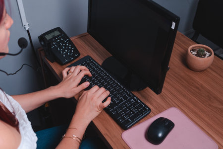 Woman working at a desk in an office with a computer. Red-haired woman working as a travel agent on the computer. High quality photoの写真素材