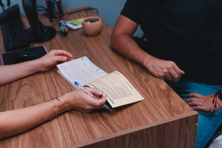 Hands of a travel agent making a sale. Two people filling out a contract at an office desk. High quality photoの写真素材