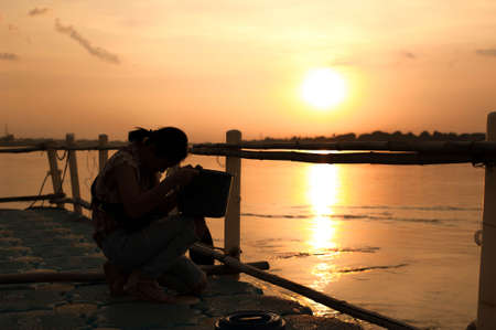 silhouette of lady make a wish for releasing fish back to Mekhong river in sunset time at Phrathat La Nong temple ,Nong Khai province Thailandの写真素材