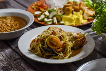 Spicy thai green papaya salad or thai name Som Tum (a famous local thai street food) with Nam Neung (Vietnamese Meatball Wraps) backgroundの写真素材