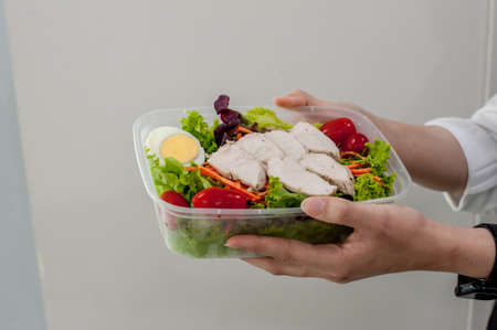 The hands hold a take away box of Chicken breast salad with boiled eggの写真素材