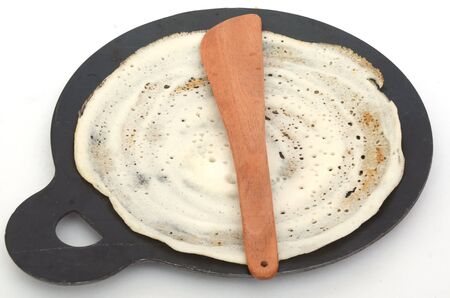 Non stick tawa with dosa and wooden spatula on an isolated white background