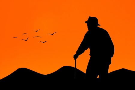 Old man walking at sunset with mountains and birds on backgroundの写真素材