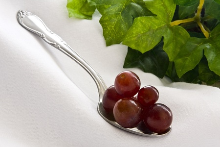 Red grapes piled on spoon on white cloth with leaves on backgroundの写真素材
