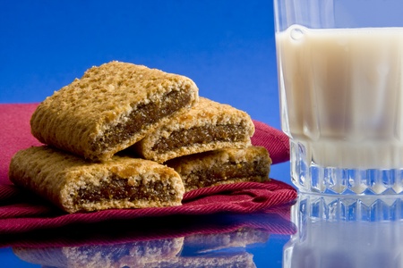 Wheat fig bars on red cloth napkin with glass of milk on blue backgroundの写真素材