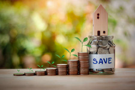 Stacking coins with trees and house model on a jar. Save money for financial and business investment...