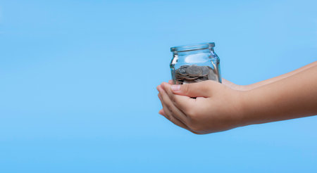 Child's hand holding a glass jar with money coin. Concept for education, save money, business, financial and funds. Background of success in the future.の写真素材