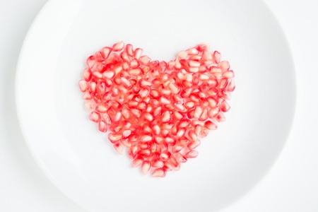 Pomegranate seeds on a white dish heart shapeの写真素材