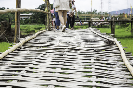 People walk on a bamboo bridge through a field to make merit at a temple in northern Thailand.の写真素材