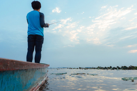 Young man fishing on a lake from old boat in the morning. Fishing concept. Light refrection on water. select focus.の写真素材
