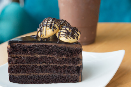Delicious chocolate cake with topping on white plate on brown table and chocolate drink