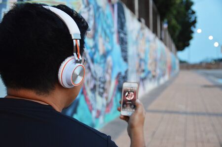 Man in wireless headphones listening to music standing on streetの写真素材