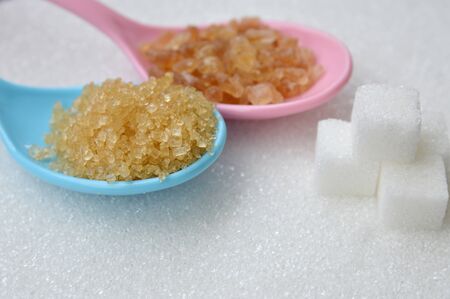 Various kinds of sugar in plastic color spoons on white sugar background. brown sugar, copyspace