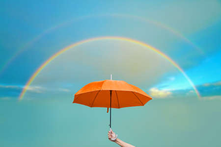 The man holding orange umbrella and two rainbows with blue sky backgroundの写真素材